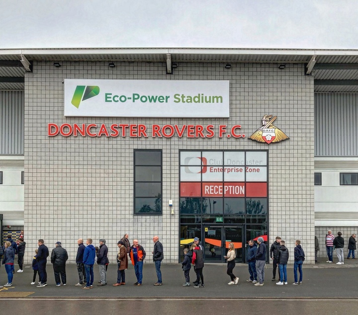 A line of football supporters queue past the main reception of Doncaster Rovers Eco-Power Stadium