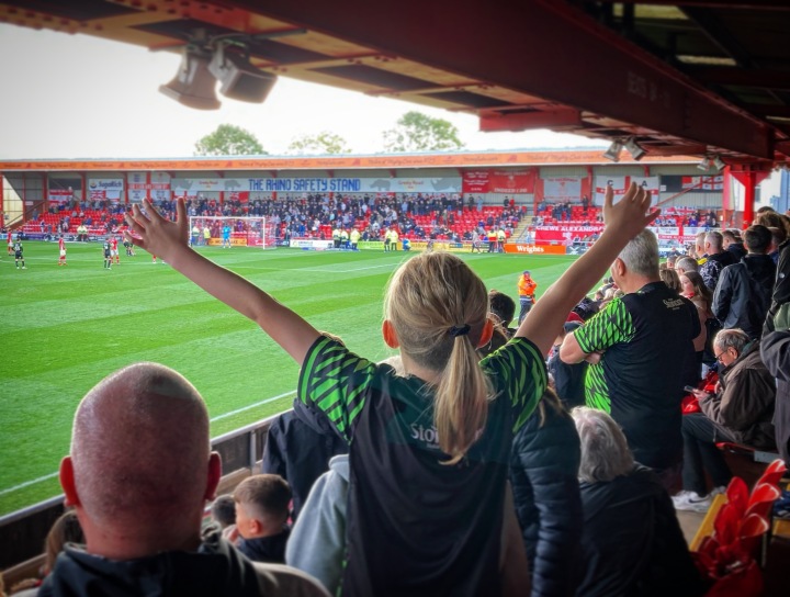 A young Doncaster Rovers fan with their arms outstretched watches her team play away at Crewe Alexandra 