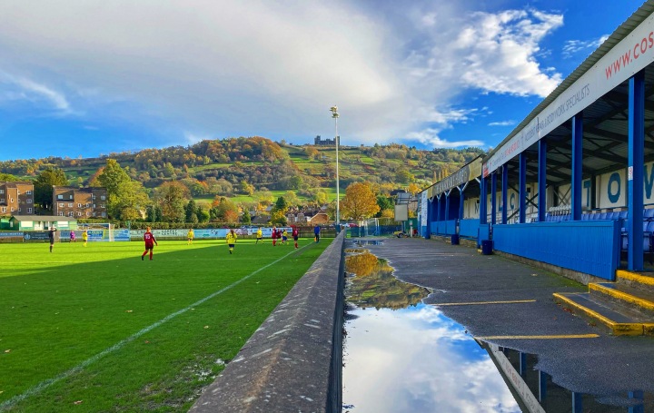 The hill behind the goal is reflected in puddles at Matlock Town's Causeway Lane ground as Matlock Town women play against Buxton