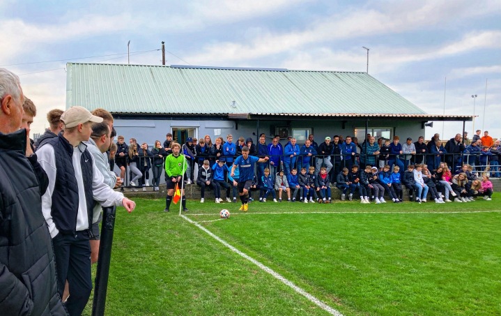 A Hakin United player takes a corner as a large number of supporters watch on 