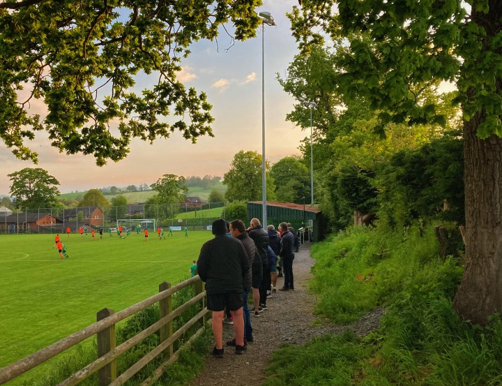 Supporters watch from the high bank at Llansantffraid's Treflan as their team play Tywyn Bryncug in an evening game