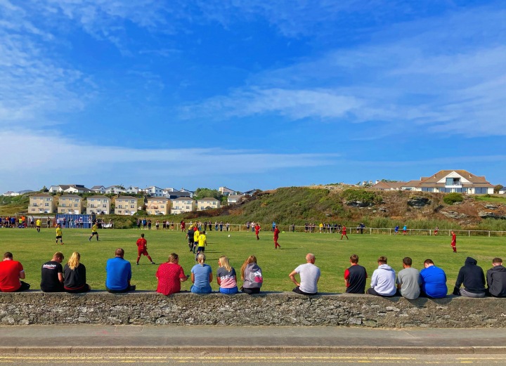 Supporters watch Trearddur Bay play Holyhead Town from on top of a stone wall